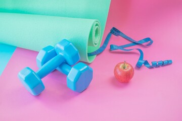 Fitness concept with dumbbells, measuring tape on bright background. Blue dumbbells and yoga mat on...
