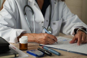 Doctor writing medical prescription with diabetes medication on desk