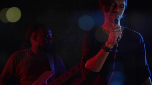 Lead singer entering red blue music stage initiating song to audience leaning mic bassist grooving