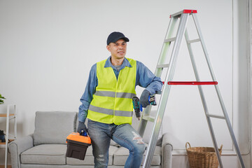 Professional male worker in safety gear standing by ladder with toolbox, preparing to perform home...