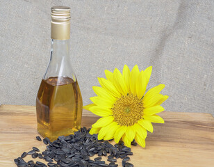 Sunflower oil in a glass bottle, sunflower seeds and sunflower flowers nearby, close-up.