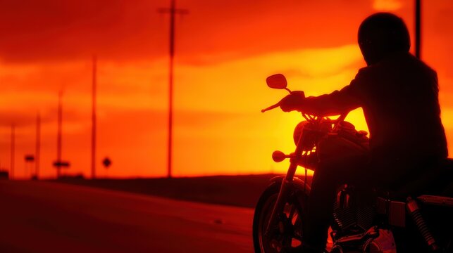 Silhouette of a motorcyclist riding into a vibrant sunset on an open road with power lines in the background