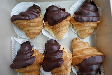 Six freshly baked chocolate croissant arranged neatly takeaway box creates delightful feeling of happiness. rich brown chocolate topping promises