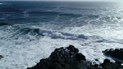 Rough sea with foamy waves crashing over dark rocks near the shore on an overcast day