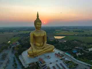 Obraz premium scenery sunset behind the great golden Buddha landmark of Thailand at wat Muang Ang Thong Thailand. The largest Buddha statue in the world Surrounded by rice fields. colorful sky background.