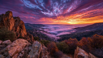 Dramatic mountain vista at fiery sunrise with fog-filled valley below