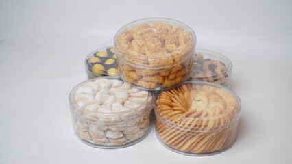 Five transparent plastic jars filled with: Nastar, Kastengel, Lidah Kucing, Putri Salju, and Chocolate Thumbprint Cookies. Each jar is neatly arranged in a row and isolated on a clean white background