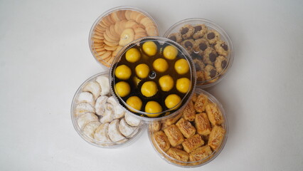 Five transparent plastic jars filled with: Nastar, Kastengel, Lidah Kucing, Putri Salju, and Chocolate Thumbprint Cookies. Each jar is neatly arranged in a row and isolated on a clean white background