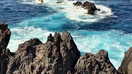 The stunningly beautiful waves are crashing vigorously against the jagged, rough rocks in a vibrant...