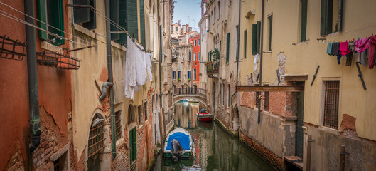 Narrow Venetian canal with bridge and hanging laundry