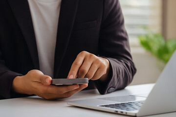 A person in a suit is using a smartphone near a laptop computer.