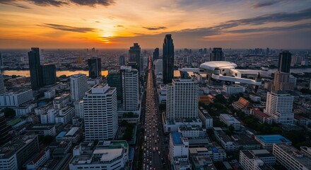 Drone flying over a bustling city at sunset, capturing an aerial view of modern skyscrapers, busy roads, and a river reflecting the golden light.