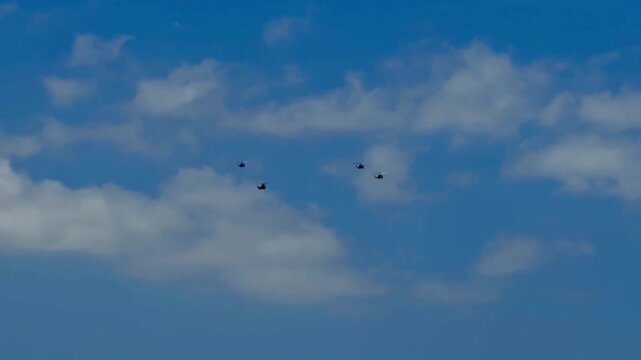 A striking view of helicopters flying in formation against a backdrop of blue skies and fluffy clouds.