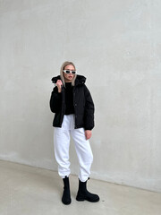 Stylish fashion ensemble featuring a woman in a black puffer jacket, white joggers, and black...