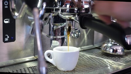 Hot coffee pouring from professional espresso machine into small white cup in Lombardy bar, ready to be served to customers