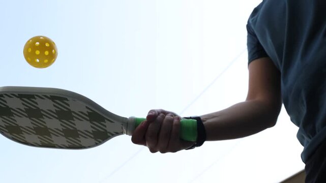 woman hitting the pickleball ball with a green pickleball paddle with the sky in the background