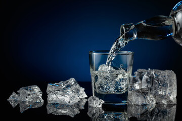 Crystal clear vodka or gin being poured over ice in a glass.