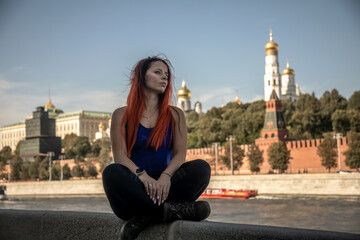 Beautiful girl sitting on the embankment. View of Moscow. Girl with red hair.