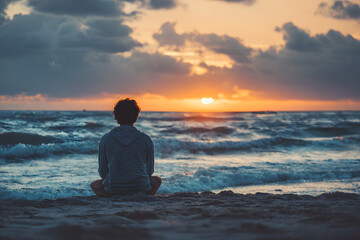 Man meditating sitting on the beach at sunset with beautiful ocean on the background.
