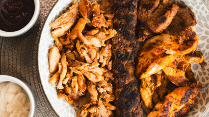 A beautifully arranged platter of grilled chicken shish, lamb shish, and doner kebab, served with vibrant sauces on the side. Elegant plating for food photography, menus, and promoting healthy, protei