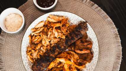 A beautifully arranged platter of grilled chicken shish, lamb shish, and doner kebab, served with vibrant sauces on the side. Elegant plating for food photography, menus, and promoting healthy, protei