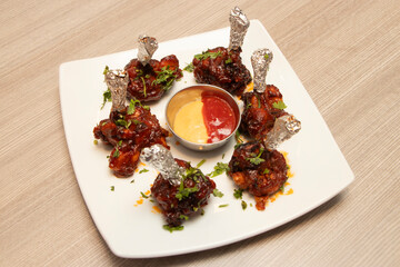 Spicy Chicken Lollipops Garnished with Fresh Herbs and Dipping Sauce in plate side view of bangladeshi food