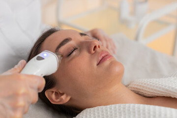 Caucasian girl receives under eye RF therapy in cosmetology clinic. Female woman cosmetologist uses...