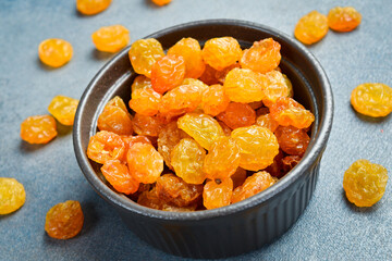 Bowl with dried golden raisins, on a stone background.