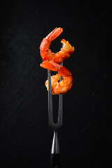 Grilled shrimp on a metal barbecue fork. On a black slate background.