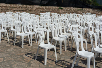 empty rows of white plastic chairs in an outdoor amphitheater. a large field of unoccupied seating...