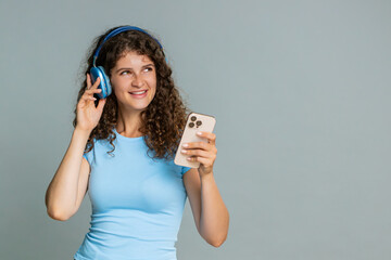 Young woman energetically dancing with smartphone wearing headphones, spinning and enjoying...