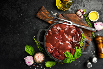 Raw fresh turkey liver in a frying pan, ready to cook. Top view. On a dark textured stone...