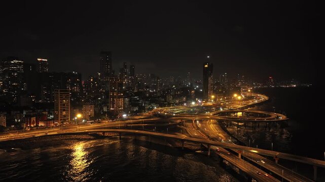 Cinematic aerial view of the Coastal road junction near Bandra Worli Sea Link in Mumbai city of Maharashtra, India, during the monsoon season at night.