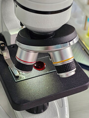 Closeup view of a microscope focusing on a glass slide with a liquid sample under examination in a...