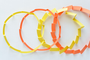 orange and yellow paper circles or rings with crimped or folded zigzag elements on blank paper