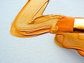 Golden metallic paint applied with a brush creating a textured stroke on canvas, depicting artistic creativity, fine arts, and vibrant design elements in a close-up studio arrangement.