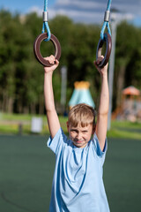 Teen boy hanging on gymnastic rings at outdoor playground