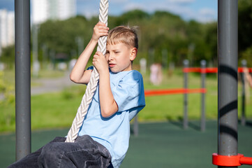 Teen boy climbing rope with effort on outdoor playground