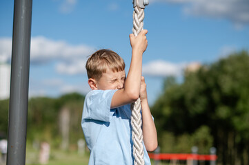 Teen boy climbing rope with effort on outdoor playground