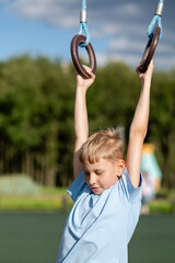 Teen boy hanging on gymnastic rings at outdoor playground