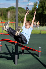 Blond teen boy swinging on gymnastic rings outdoors
