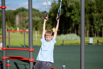 Blond teen boy swinging on gymnastic rings outdoors