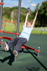 Blond teen boy swinging on gymnastic rings outdoors