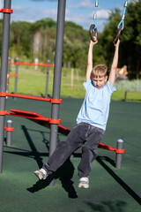 Blond teen boy swinging on gymnastic rings outdoors