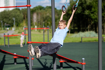 Blond teen boy on gymnastic rings outdoors