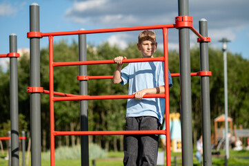 Teen boy climbing sports ladder on playground with sports equipment