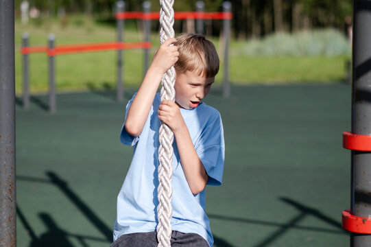 Teen boy climbing rope with effort on outdoor playground
