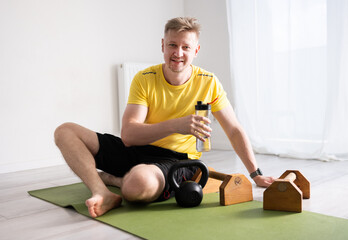 Happy Smiling Sporty Man Sitting On The Floor At Home Relaxing After Morning Sport Routine