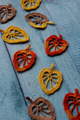 Handmade crocheted autumn leaves arranged on vintage blue wooden surface. Ideal for creative design, fall decor, DIY inspiration, knitting tutorials, seasonal crafts, rustic background projects.