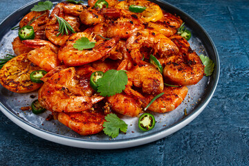 grilled shrimp, unpeeled, headless, with spices, on a dark blue table, homemade, no people,